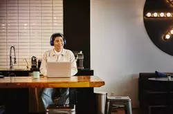 Man with headphones working on laptop at a table in a cafe